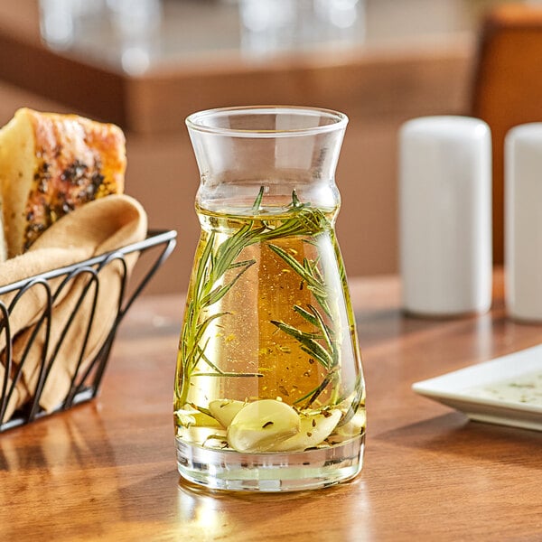 An Arcoroc Fluid Carafe filled with liquid on a table with a basket of bread.