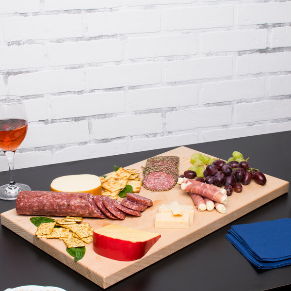 A Vollrath hardwood display cutting board with meats and cheese on it on a table.