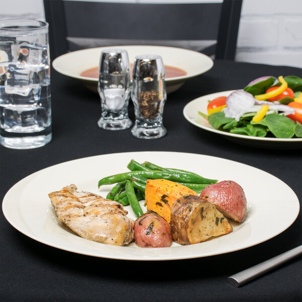 A 10 Strawberry Street Royal Cream porcelain dinner plate with food on it next to a glass of water.