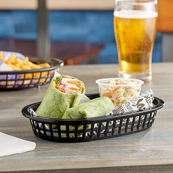 A black Tablecraft oval plastic fast food basket with food in it on a table.