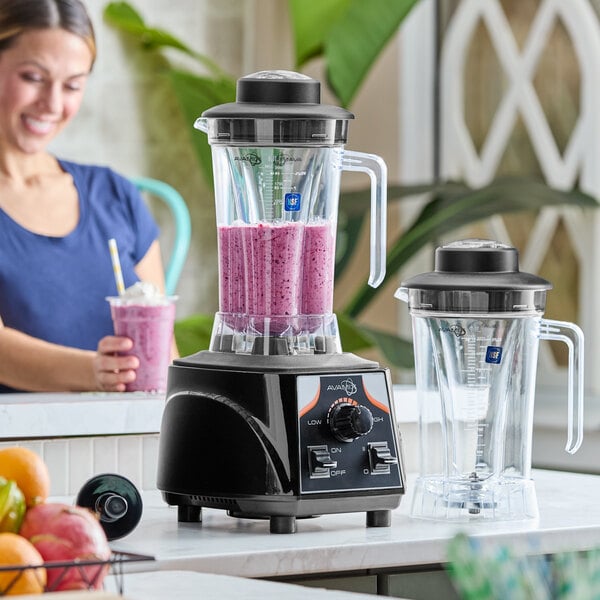 A commercial blender with a black base, toggle controls, and two clear 64 oz. containers, one filled with a purple smoothie.