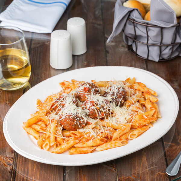 An oval ivory porcelain platter with a plate of pasta with meatballs and cheese on it.