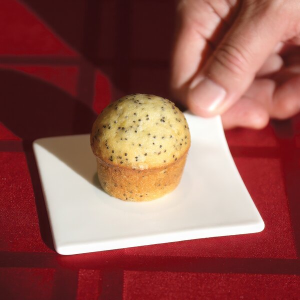 A hand holding a small muffin on a Libbey Chef's Selection II porcelain plate.