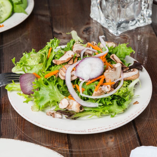 A Libbey Farmhouse ivory porcelain plate with a salad with vegetables and mushrooms on it.