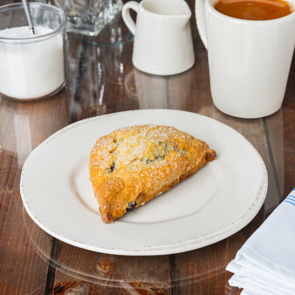 A Libbey Farmhouse wide rim porcelain plate with a scone on it next to a cup of coffee.