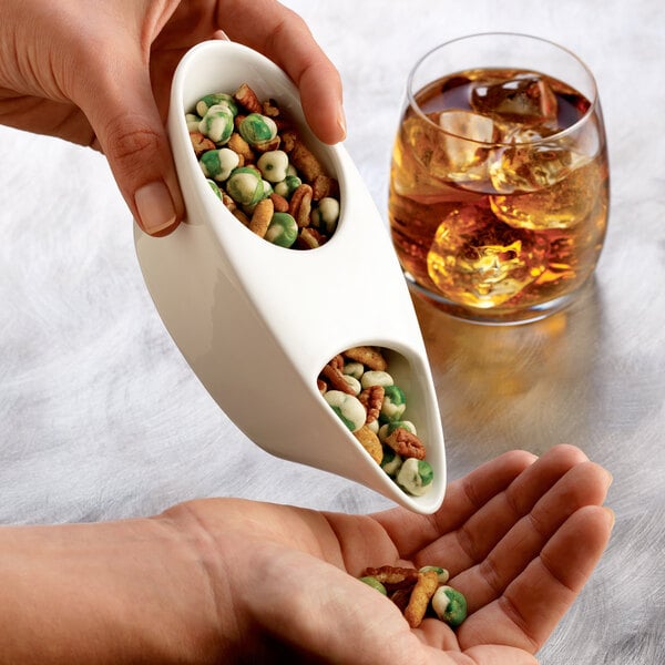 A person pouring nuts from a Libbey porcelain bar snack dispenser into a bowl.