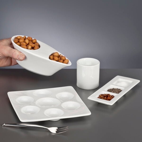 A person holding a Libbey ultra bright white porcelain bar snack dispenser filled with peanuts.