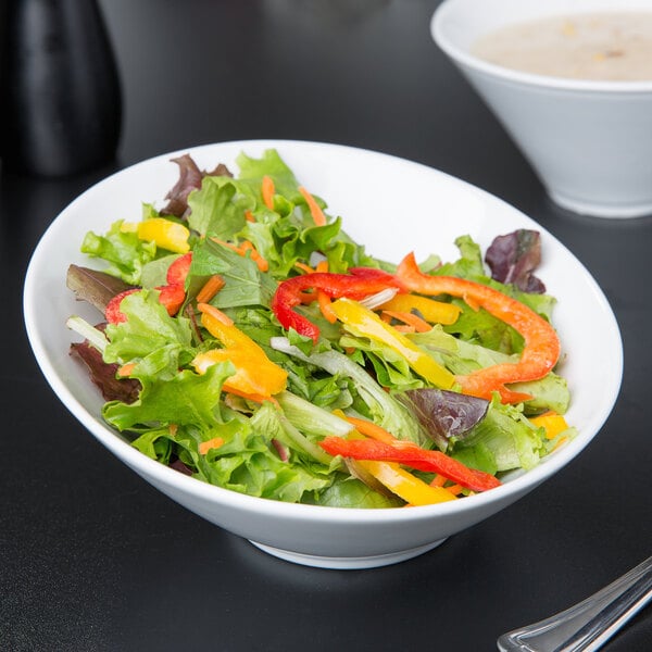 A Libbey white porcelain bowl filled with salad and peppers on a table with a bowl of soup.