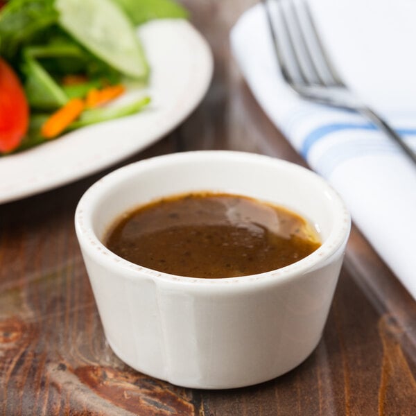 A Libbey ivory porcelain sauce bowl filled with brown sauce on a table with a salad plate.