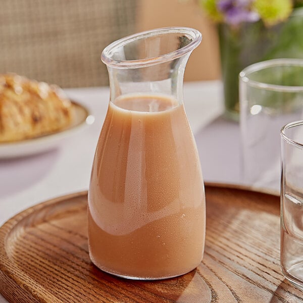 A Carlisle polycarbonate carafe of liquid on a wooden tray with a plate of food on a table in a brunch café.