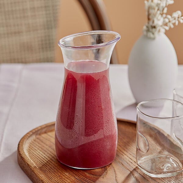 A Carlisle polycarbonate carafe filled with red liquid on a wooden tray.