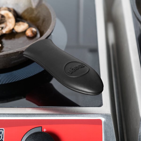 A Lodge mini silicone handle holder on a pan with mushrooms cooking on a stove.