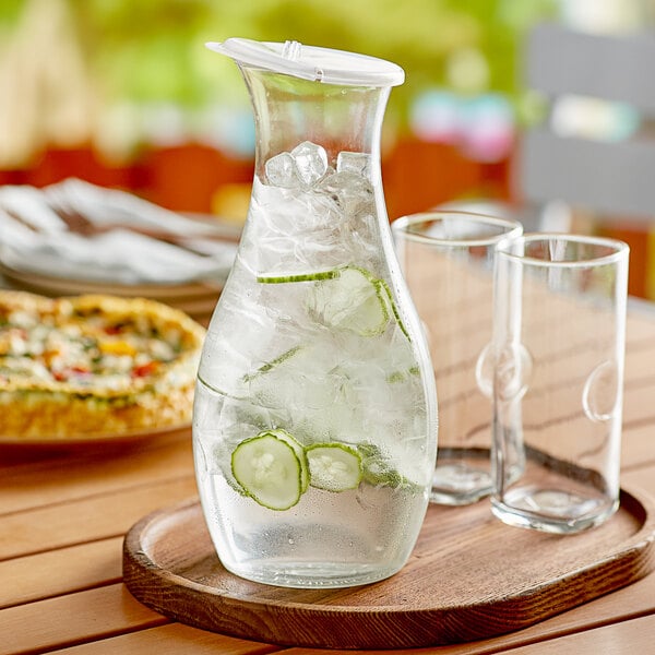 A Carlisle polycarbonate carafe with ice water and cucumber slices on a wooden tray.