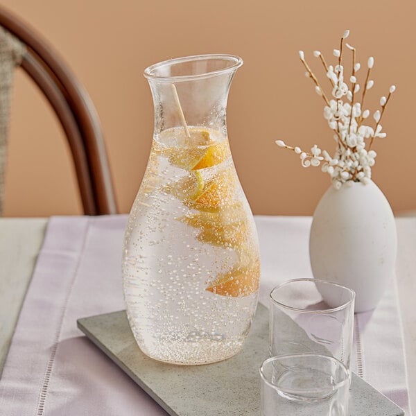 A Carlisle polycarbonate carafe with a drink and orange slices on a table.