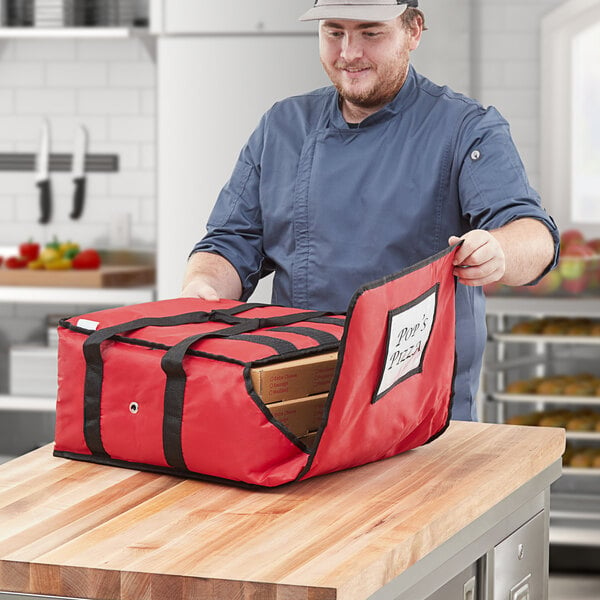 A man in a chef's hat opening a red CaterGator pizza delivery bag with boxes inside.