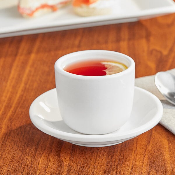 An Acopa bright white stoneware tea cup with a lemon slice on a saucer.