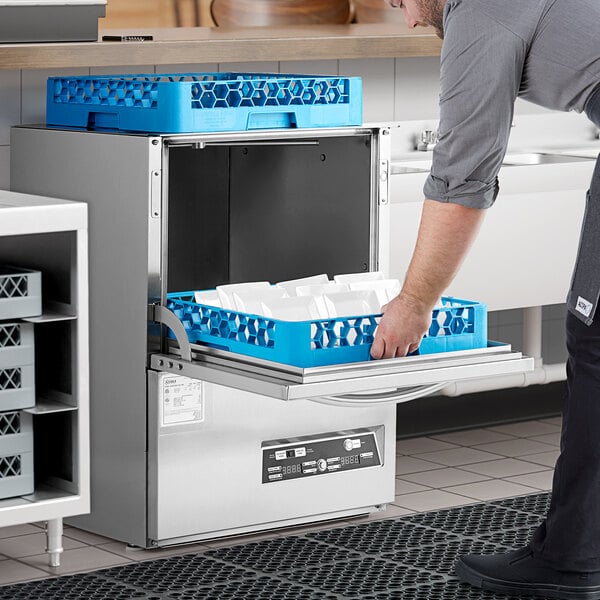 A man opening a Noble Warewashing undercounter dishwasher on a professional kitchen counter with a blue tray.