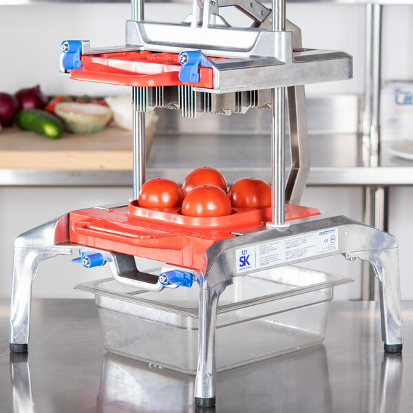A Prince Castle Saber King tomato slicer blade assembly on a machine with tomatoes.