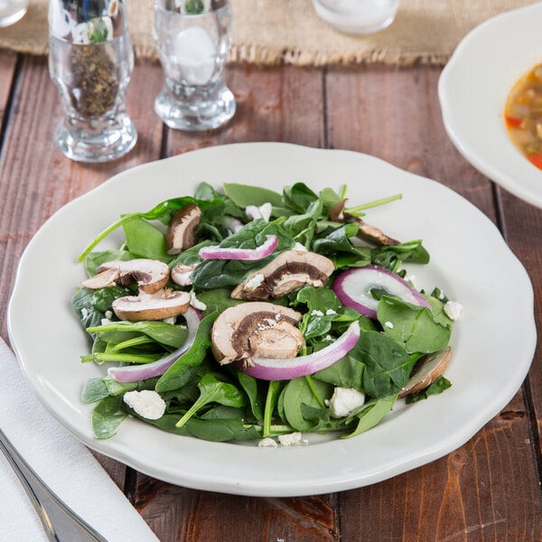 A Tuxton ivory china plate with a salad of spinach, mushrooms, and onions.