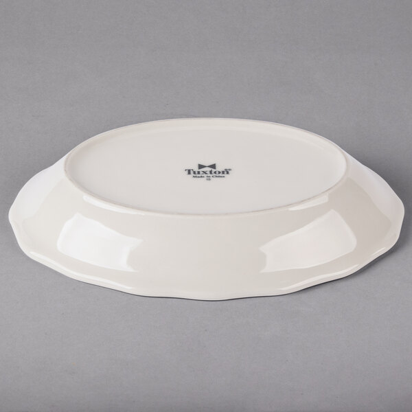 A white Tuxton oval china platter with a scalloped edge.