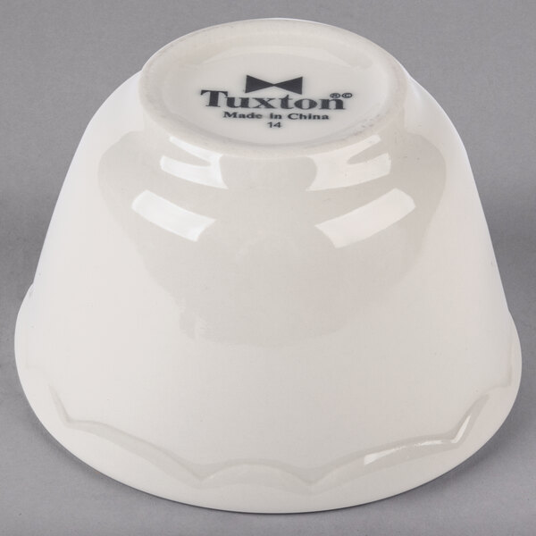 A white Tuxton China bouillon cup with black scalloped text on it.