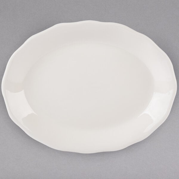 A white Tuxton oval china platter with a scalloped edge.