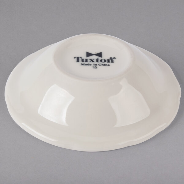 A white Tuxton china bowl with black scalloped edges and black text on it.