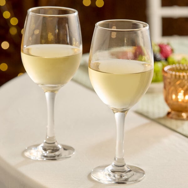 A pair of clear, stemmed wine glasses filled with white wine on a table.
