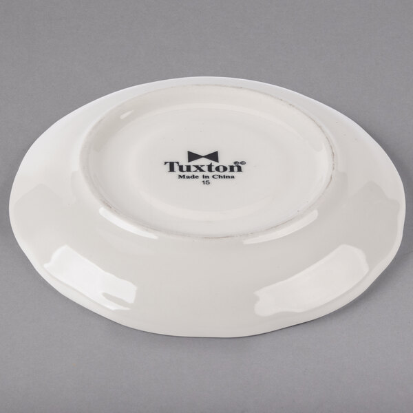 A white Tuxton saucer with black scalloped edges and black text that reads "Tuxton China"