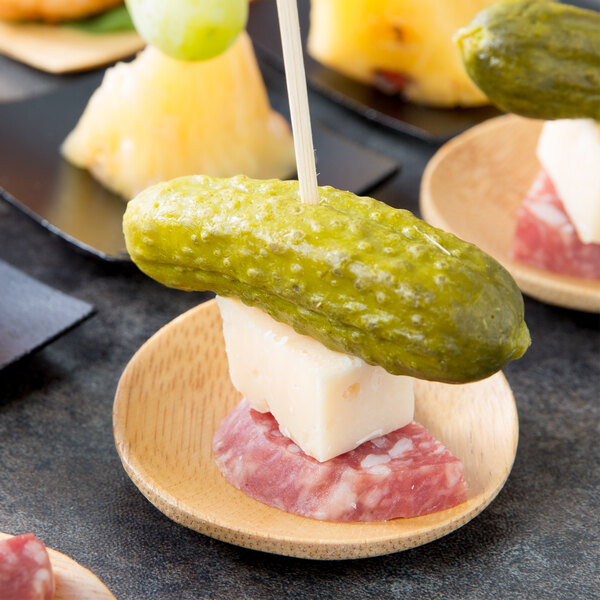 A Tablecraft bamboo round dish with food on it, including a pickle on a stick.