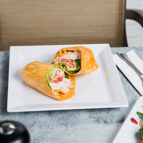 A white Elite Global Solutions square melamine plate with a sandwich and salad on it, with a fork and knife on a napkin.