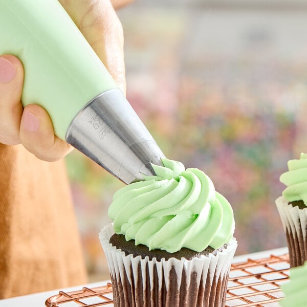 An open star piping tip being used to decorate a cupcake with green frosting.