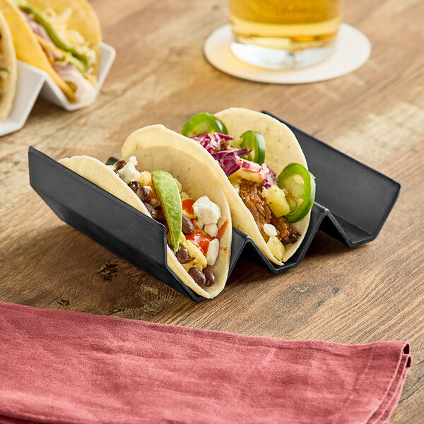 A black Elite Global Solutions taco stand holding three tacos on a table.