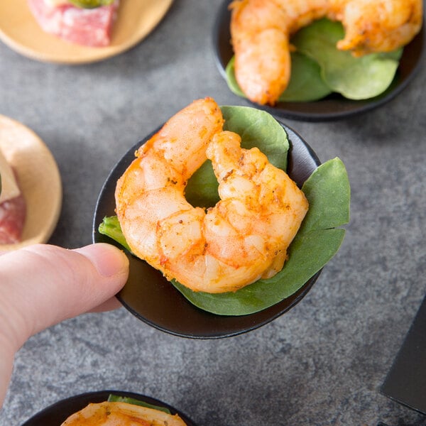 A hand holding a Tablecraft black bamboo dish with shrimp on it.