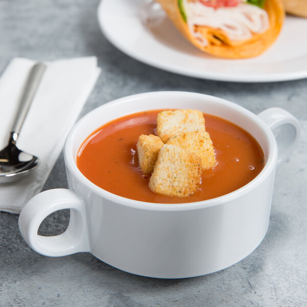 A white bowl of soup with croutons and bread on the side.