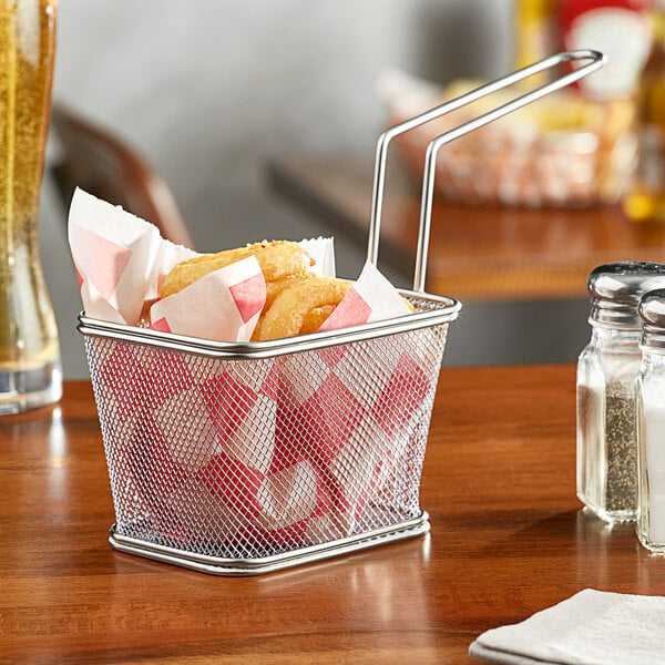 A Clipper Mill stainless steel single serving fry basket with fried food on a table.