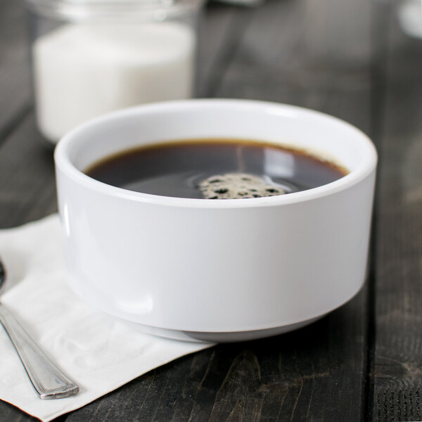 A white Elite Global Solutions melamine cup filled with coffee on a table with a napkin and a spoon.