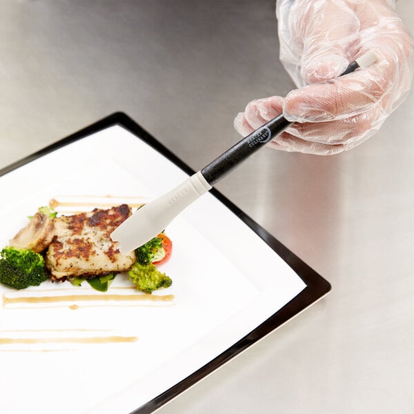 A person using a Mercer Culinary silicone brush to plate food.