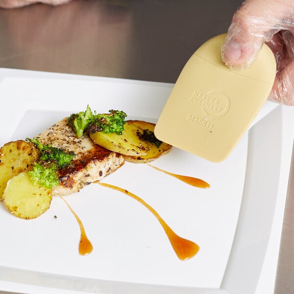 A person using a Mercer Culinary silicone wedge to plate food.