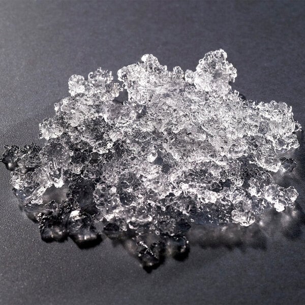 A pile of clear, irregularly shaped flake ice pieces on a dark surface.