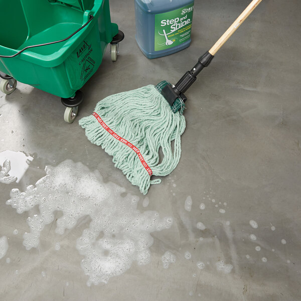 A green Rubbermaid mop head in a bucket of soapy water on the floor.