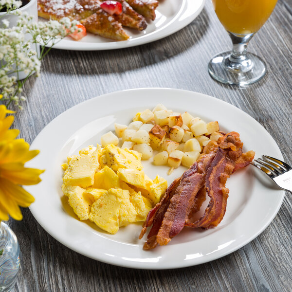 A Libbey white porcelain plate with eggs, bacon, and potatoes on a table.