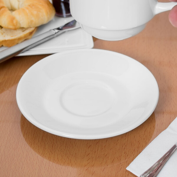 A hand holding a white Libbey porcelain tea saucer under a white cup.