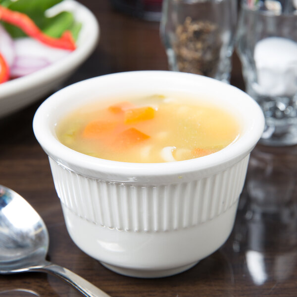 A Tuxton Hampshire eggshell embossed china bouillon cup filled with soup on a table with a spoon