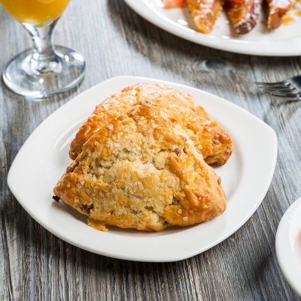 A white Libbey Slenda porcelain plate with a plate of scones and pastries on a table.