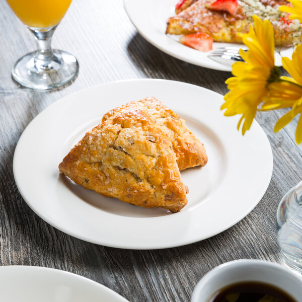 A Libbey Royal Rideau white porcelain plate with pastries on a table with a glass of juice.