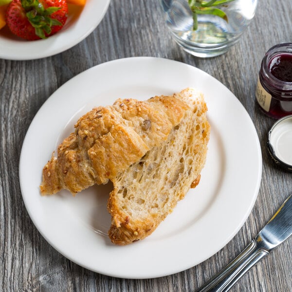 A Libbey white porcelain plate with a croissant on it next to a bowl of fruit.