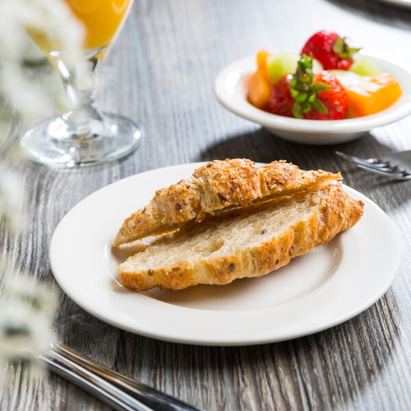 A Libbey white porcelain plate with a croissant and fruit on it on a table.