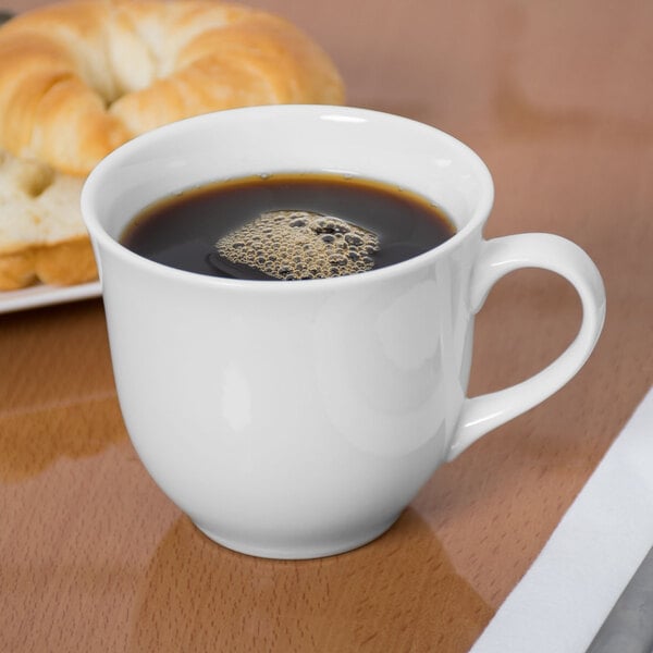 A Libbey Royal Rideau white porcelain cup of coffee next to a bagel.