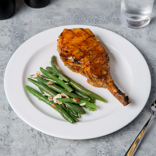 A Libbey round white porcelain plate with a piece of chicken and green beans on it.